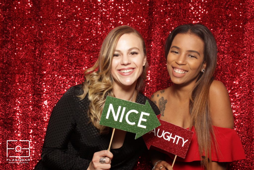 Two women with Nice and Naughty props at a Flashbar holiday photo booth