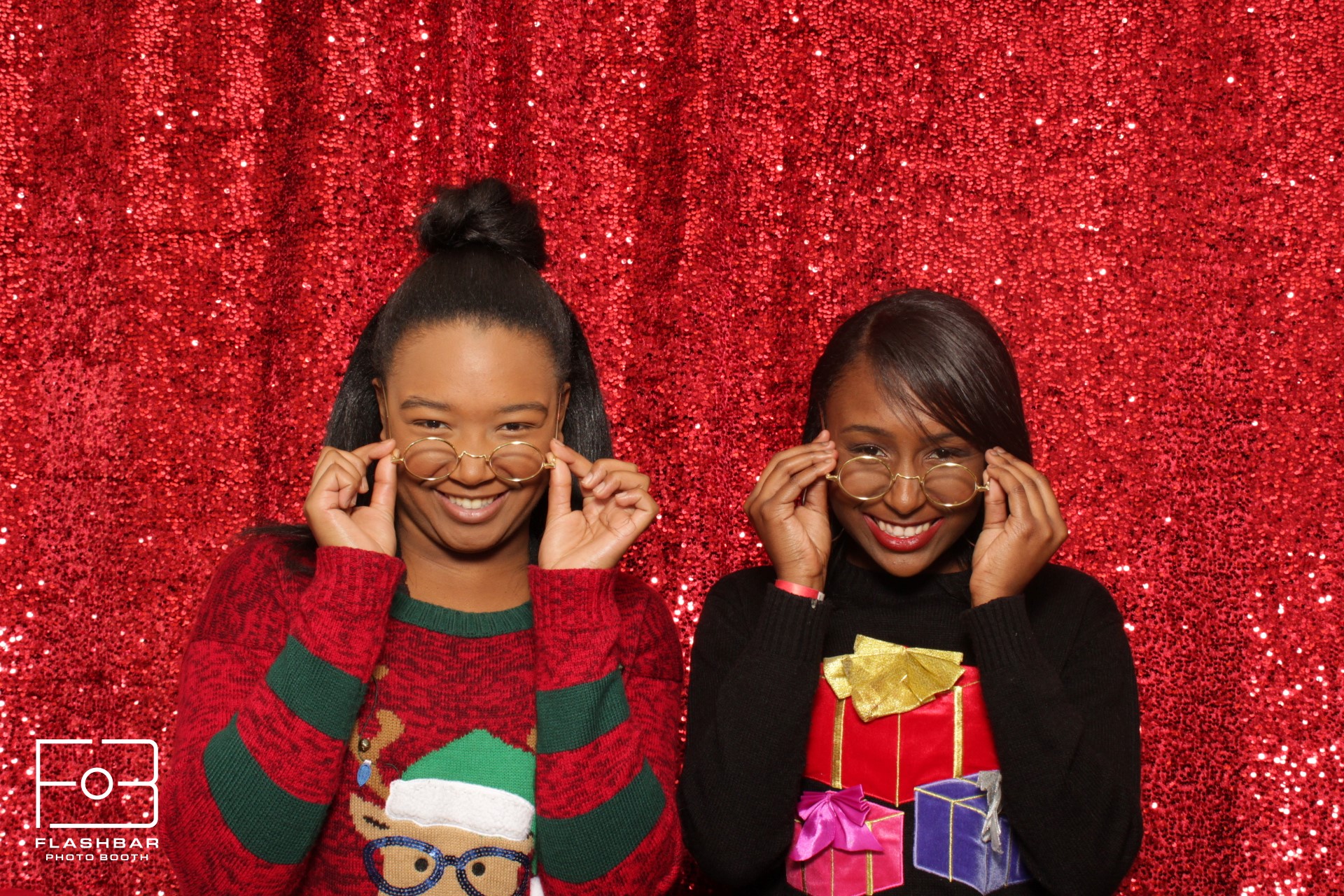 Two women in holiday sweaters posing at a Flashbar holiday photo booth