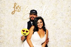 Couple posing with props at a floral-wall Flashbar photo booth