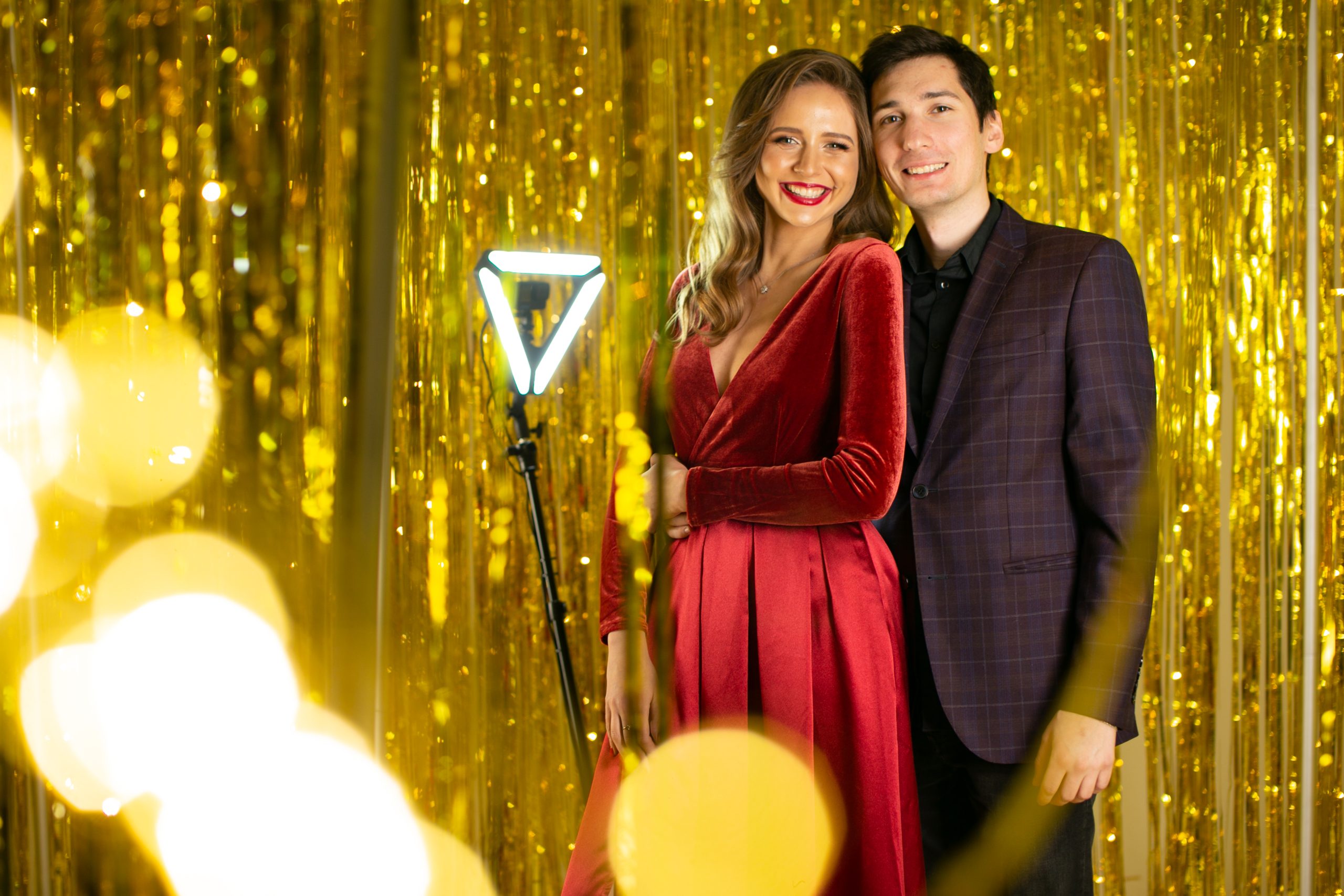 Couple posing on a 360 photo booth platform with a gold tinsel backdrop