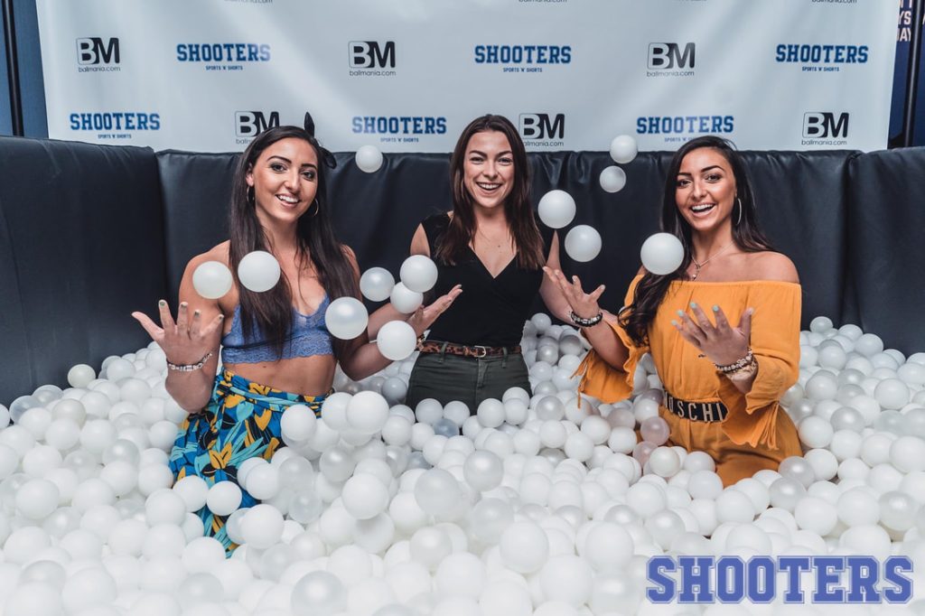 Three women posing in a Flashbar ball pit photo booth with a Shooters branded backdrop