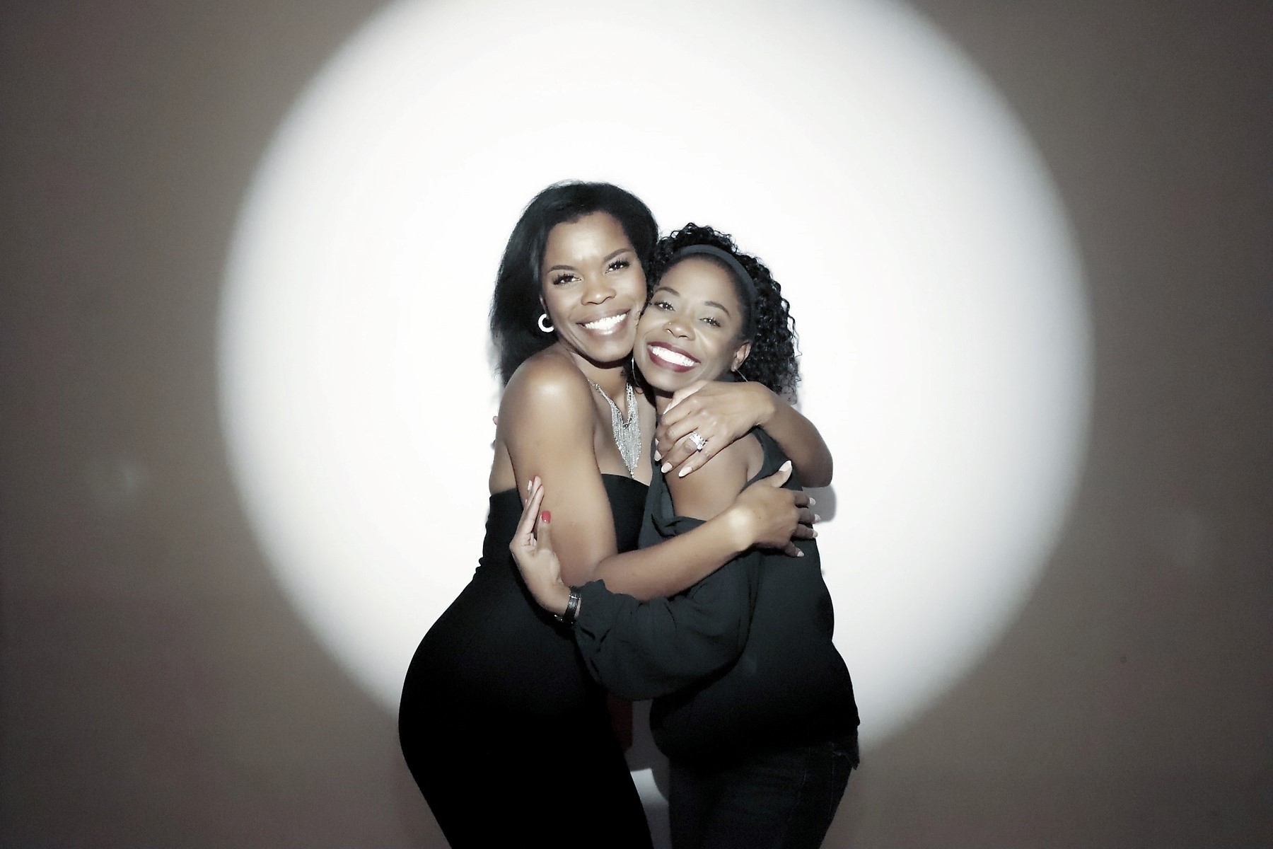 Two women embracing under a spotlight at a Flashbar photo booth
